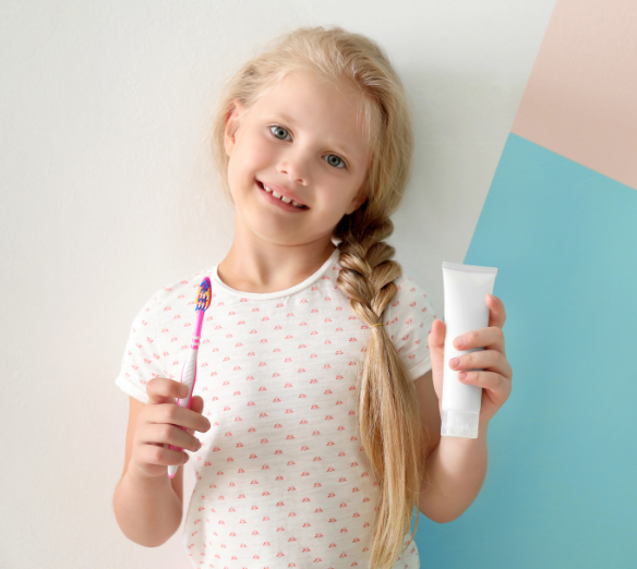 niña sujetando un cepillo de dientes y una pasta dental